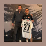 Tim Stracke und Mario Götze stehen nebeneinander, Mario Götze hält ein Trikot mit der Nummer 27